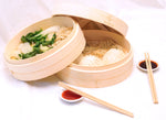 Bamboo steamer with vegetable on one tray and dumplings on another. Chopsticks and sauce also shown